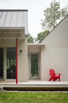 a red chair sitting on top of a wooden deck in front of a white house