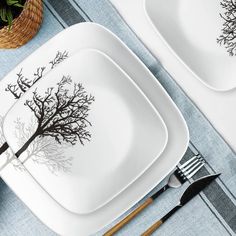 two white plates with black tree designs on them and silverware next to each other