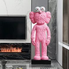 a large pink teddy bear sitting in front of a fireplace