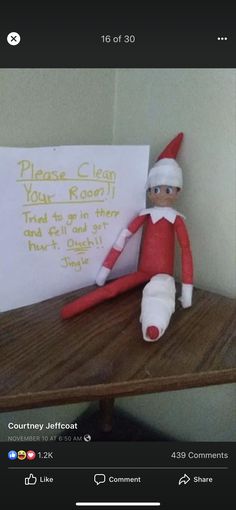 an elf is sitting on a desk with a sign in front of him that says please clean your room