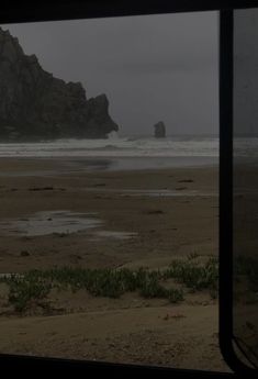 a view out the window of a train looking at an ocean and rock formation in the distance