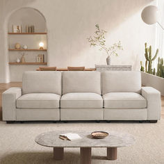 a living room with a white couch and coffee table in front of a potted plant