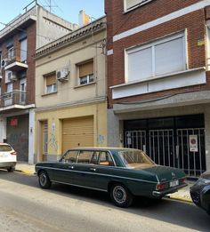 an old car is parked on the side of the street in front of apartment buildings