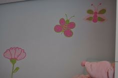 a pink stuffed animal sitting on top of a bed next to a wall with butterflies and flowers