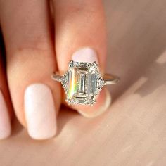 a woman's hand holding a ring with an emerald and diamond center stone on it