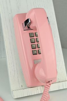 an old pink telephone sitting on top of a wooden shelf next to a white wall