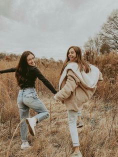 two girls are running through the tall grass together, one is carrying a backpack and the other has her arms out