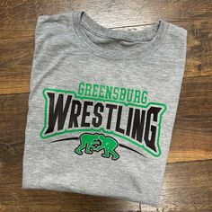 a grey tshirt with green and black wrestling on the front that says greensburg wrestling