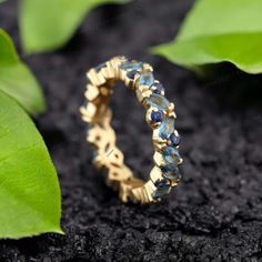 a gold ring with blue stones sitting on top of a green leafy plant next to it