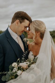 a bride and groom standing close together in front of the camera with an overcast sky behind them