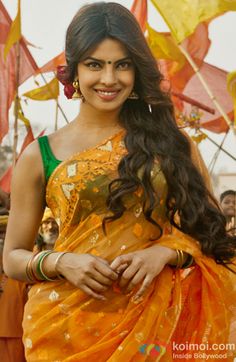 a woman in an orange and yellow sari with long hair smiling at the camera