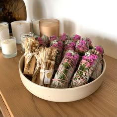 a white bowl filled with lots of different types of flowers next to candles on a table