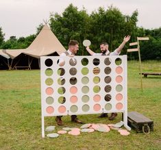 two men standing in front of a giant board game on the grass with their hands up