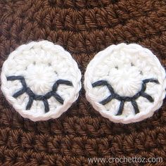 two white crocheted buttons with black eyes on brown fabric, sitting on top of each other