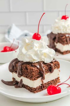 two pieces of chocolate cake with whipped cream and cherries on top, sitting on a white plate