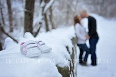 a couple kissing in the snow with their shoes on a stone wall next to them