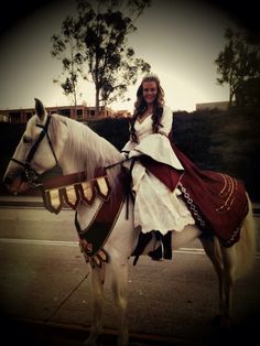 a woman in white dress riding on the back of a white horse with red and gold accents