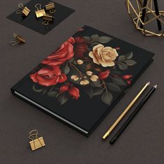 an open notebook with flowers on it next to gold pen and other items that include pens