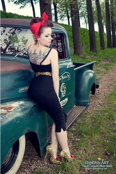 a woman sitting on the back of an old green truck with a red bow in her hair