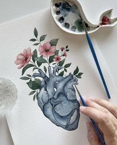 someone is painting a heart with flowers and leaves on the paper next to a spoon