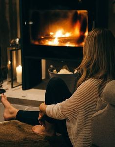 a woman sitting on the floor in front of a fire place with her feet up