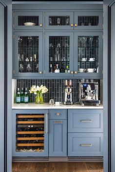 a kitchen with blue cabinets and white counter tops in front of a wine rack filled with bottles