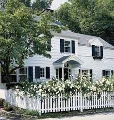 a white house with black shutters and flowers on the fence