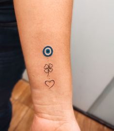 an evil eye and clover tattoo on the left inner arm, with hearts in the middle