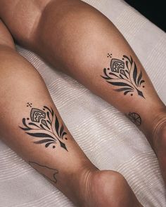 two people with tattoos on their legs sitting on a white bed and one has black ink