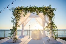 an outdoor wedding setup with white flowers and greenery on the side of the ocean