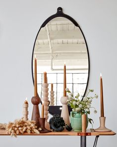 a mirror sitting on top of a wooden shelf next to candles and flowers in vases