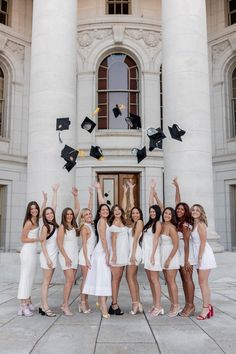 a group of women in white dresses and graduation caps throwing their hats in the air