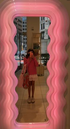 a woman taking a selfie in front of a pink mirror with wavy lines on it