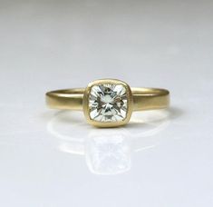 a yellow gold engagement ring with a square cut diamond in the center, on a white background