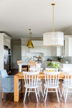 a dining room table with white chairs and a light fixture hanging from it's ceiling