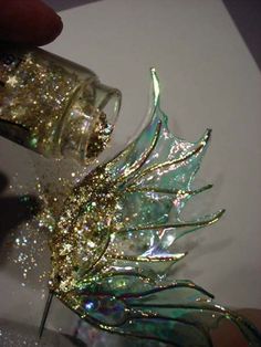 a hand is holding a small glass object with glitter on it's wings and leaves