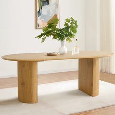 a wooden table sitting on top of a white rug next to a vase filled with green plants