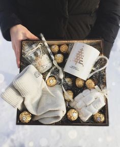 a person holding a box filled with chocolates, coffee and mittens in the snow