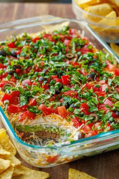 a casserole dish filled with lots of vegetables and toppings next to tortilla chips