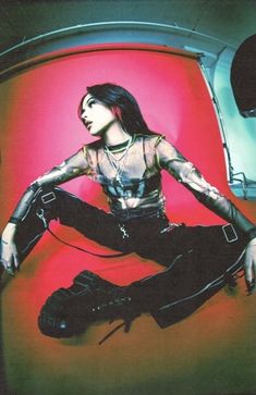 a woman sitting on top of a red chair wearing black leather pants and boots with her hands in her pockets