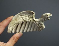 a hand holding a comb with an animal shaped like it's head and wings