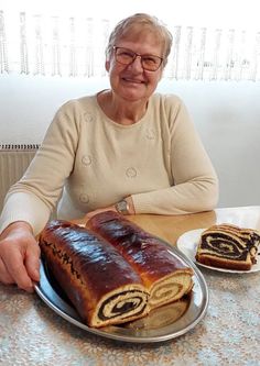 an older woman sitting at a table with a large loaf of bread in front of her