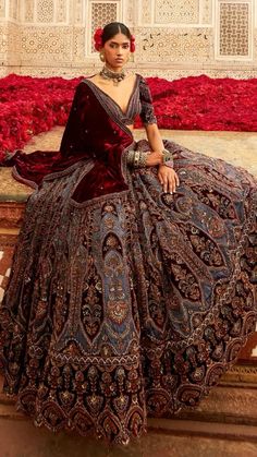 a woman in a long dress sitting on a ledge with red flowers behind her and wearing jewelry