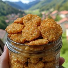 a person holding a jar filled with cookies on top of a wooden table next to a window