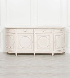 a white sideboard with three doors and two drawers on the bottom, in an empty room