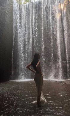 a woman standing in front of a waterfall with her back to the camera and arms behind her head