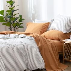 an unmade bed with orange and white striped comforters on it, next to a potted plant