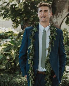 a man in a suit and tie standing under a tree with greenery around his neck