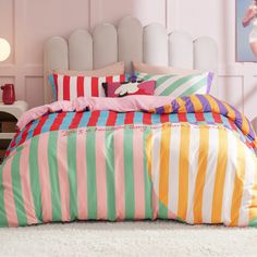 there is a bed with colorful striped sheets and pillows on it in the room that has pink walls