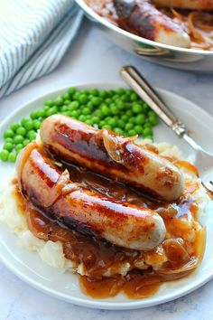 two sausages with gravy and mashed potatoes on a plate next to peas